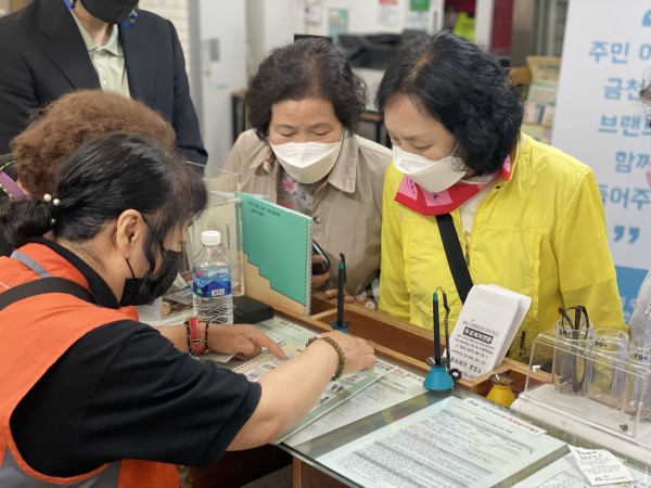 독산1동 주민센터에 비치된 그림글자판을 보며 오늘 발급해볼 서류가 무엇인지 설명하는 AAC 모니터링단원과 경청하는 금정구장애인복지관 참여자들