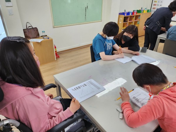 직사각현 테이블에 앉아 낱말긋기로 자음 공부를 하고 있는 이용자 사진