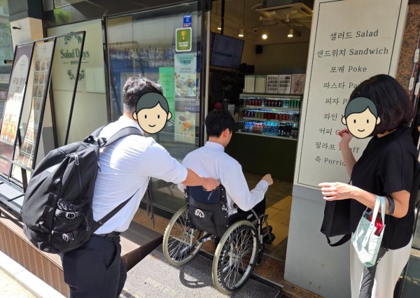 휠체어를 타고 키오스크를 이용해보는 임직원 탐사대의 모습